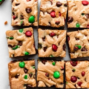 sliced M&M cookie bar squares on parchment with chocolate chips and Christmas M&Ms.