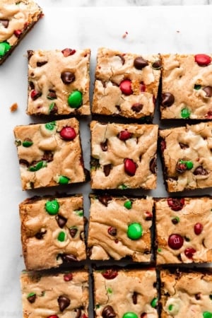 sliced M&M cookie bar squares on parchment with chocolate chips and Christmas M&Ms.