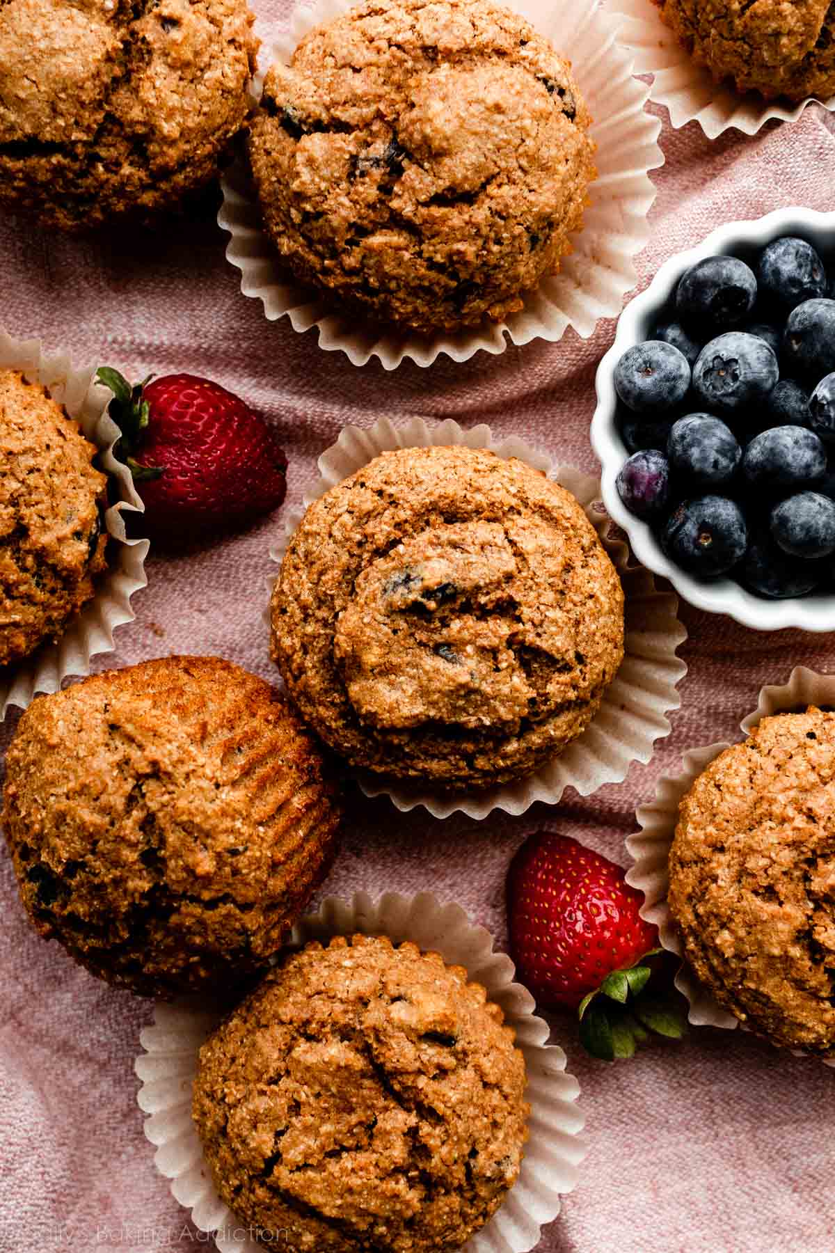 bran muffins with strawberries and bowl of blueberries next to them.