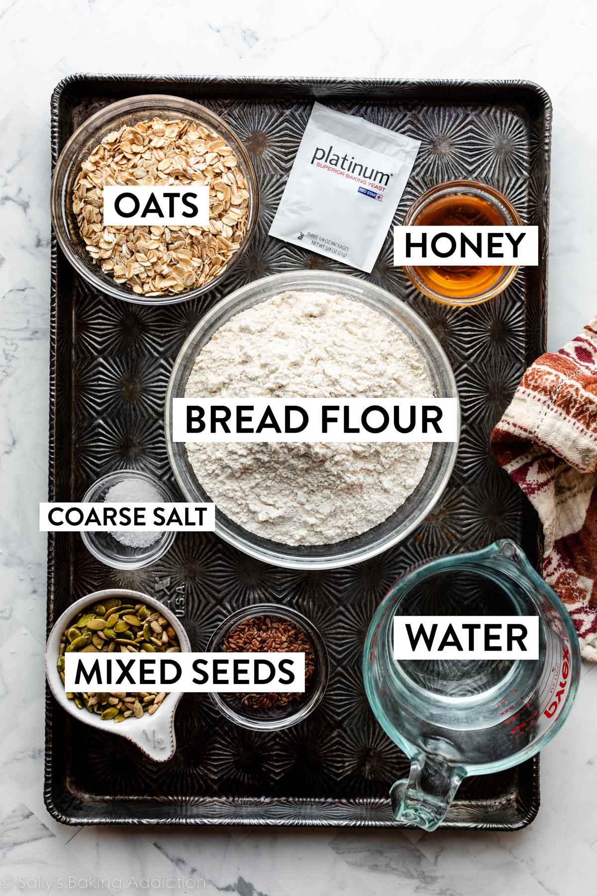 bread flour, honey, yeast, oats, seeds, and other ingredients on baking tray.