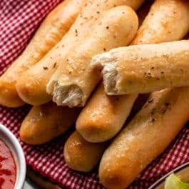 breadstick broken in half on top of other breadsticks wrapped in red checkered linen.