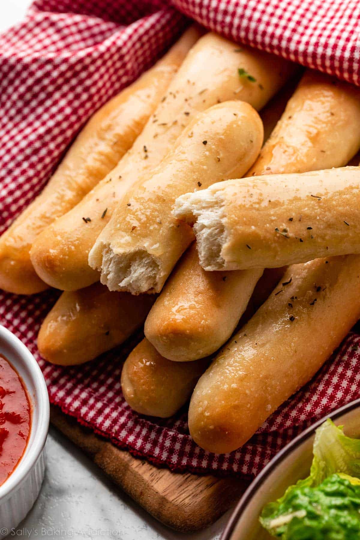 breadstick broken in half on top of other breadsticks wrapped in red checkered linen.