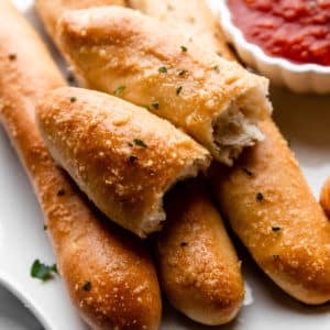 breadstick broken in half on top of other breadsticks on plate with marinara sauce.