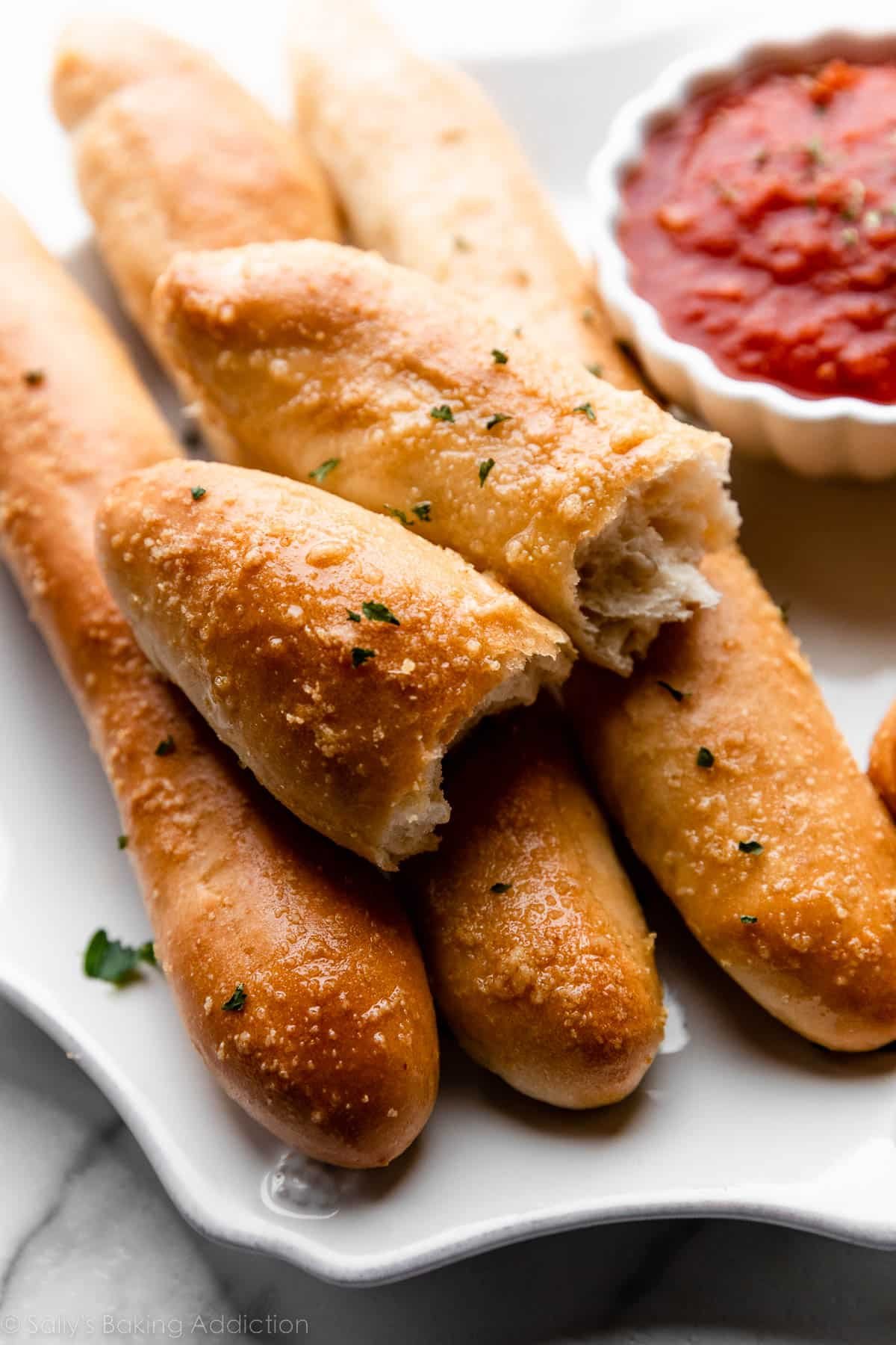 breadstick broken in half on top of other breadsticks on plate with marinara sauce.