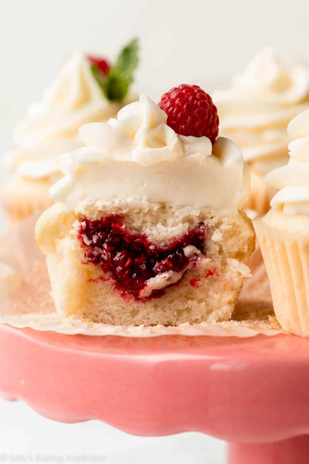 vanilla cupcake with white chocolate frosting cut open to show raspberry filling.