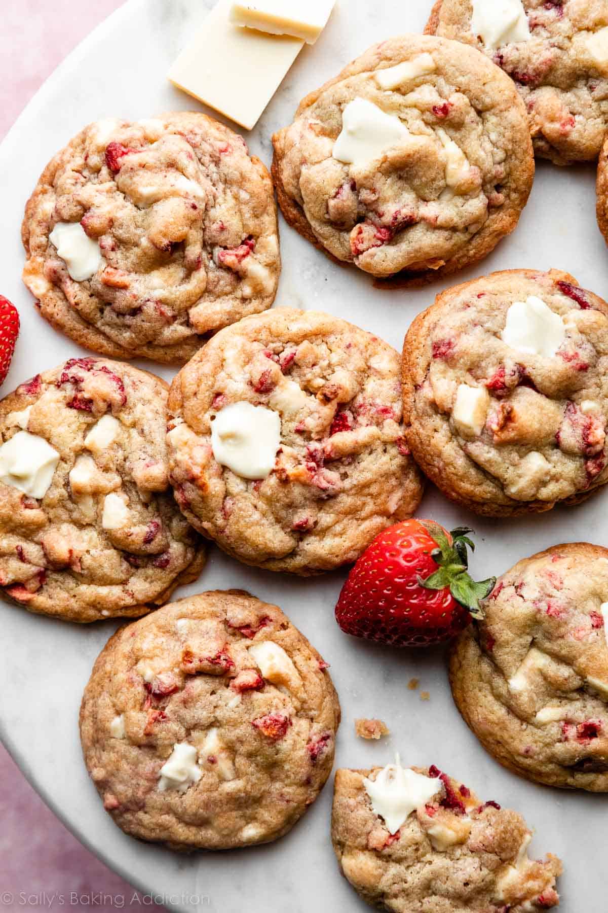 white chocolate strawberries & cream cookies on marble backdrop with fresh strawberry and white chocolate chunks.