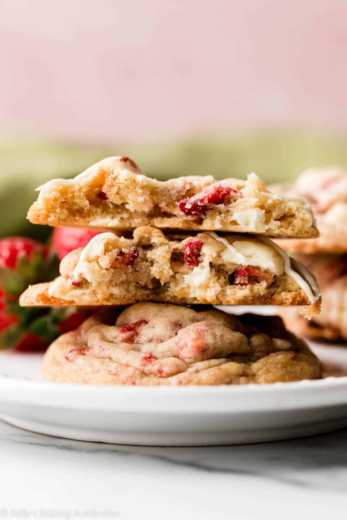 stack of white chocolate strawberries and cream cookies with top cookie broken in half.