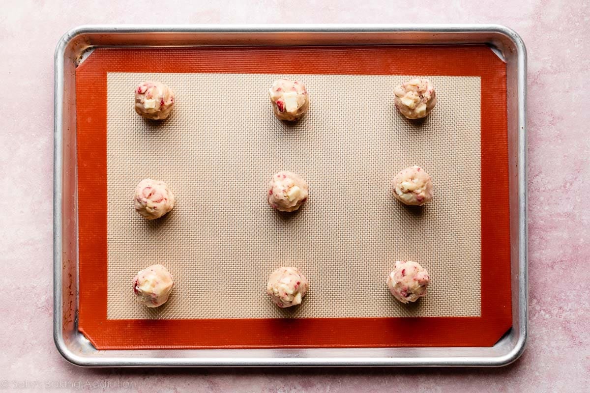 strawberry white chocolate cookie dough balls arranged on silicone baking mat-lined baking sheet.