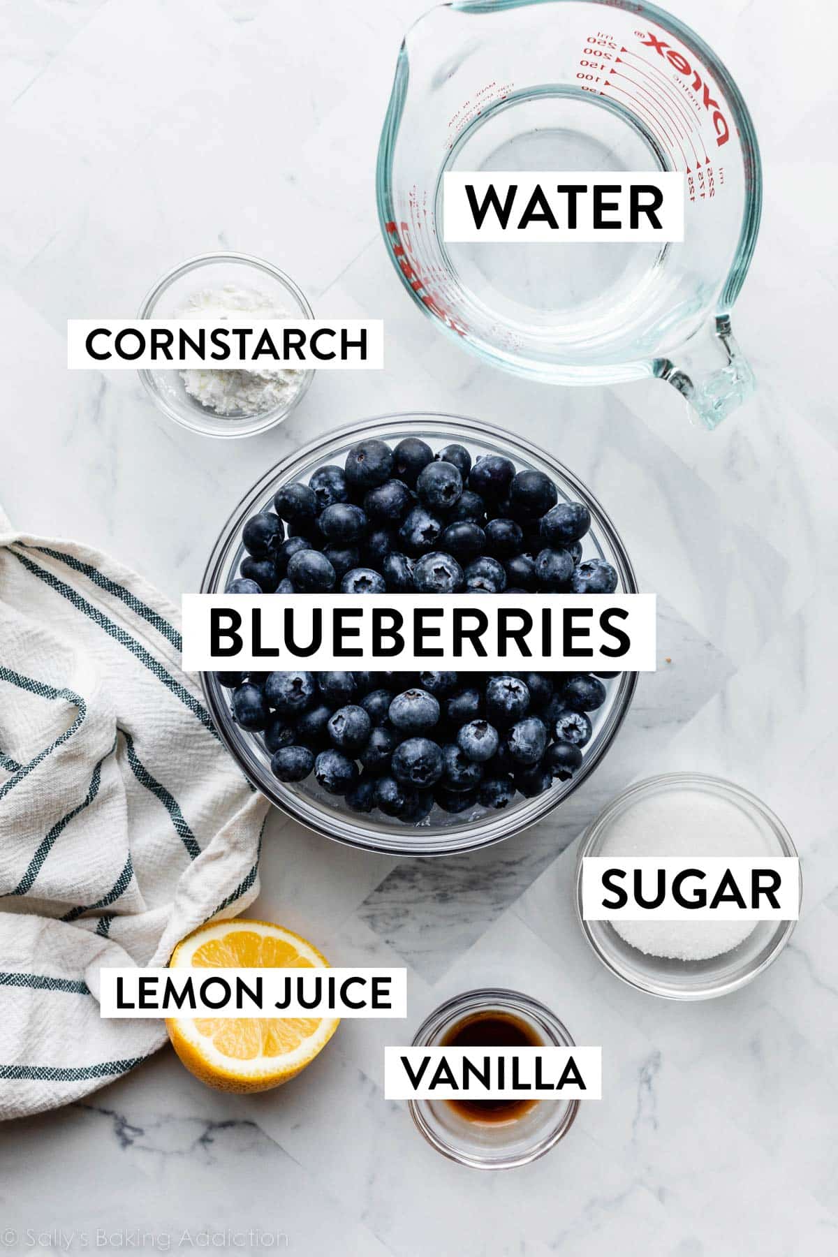 ingredients on marble counter including blueberries, water, lemon, cornstarch, sugar, and vanilla extract.