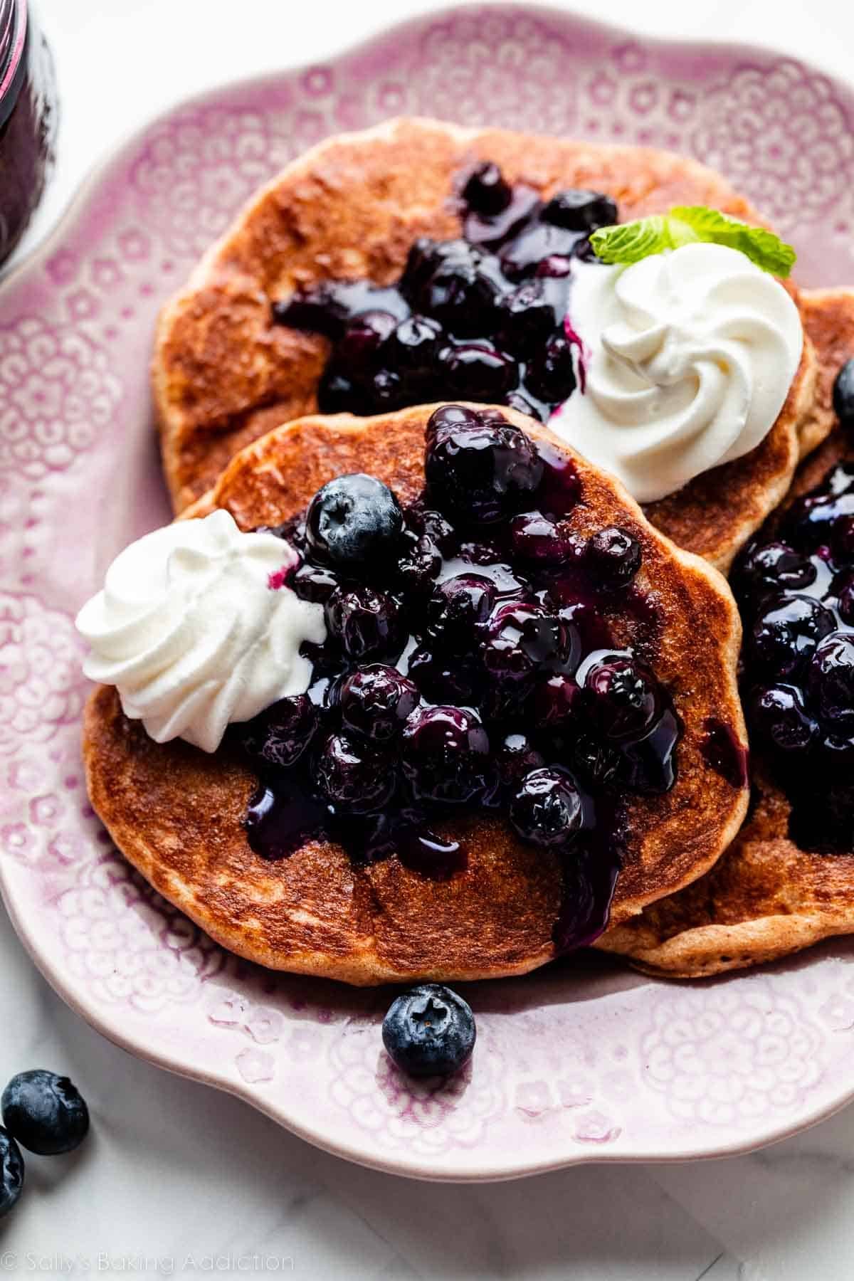 whole wheat pancakes with blueberry sauce topping and piped whipped cream on top.