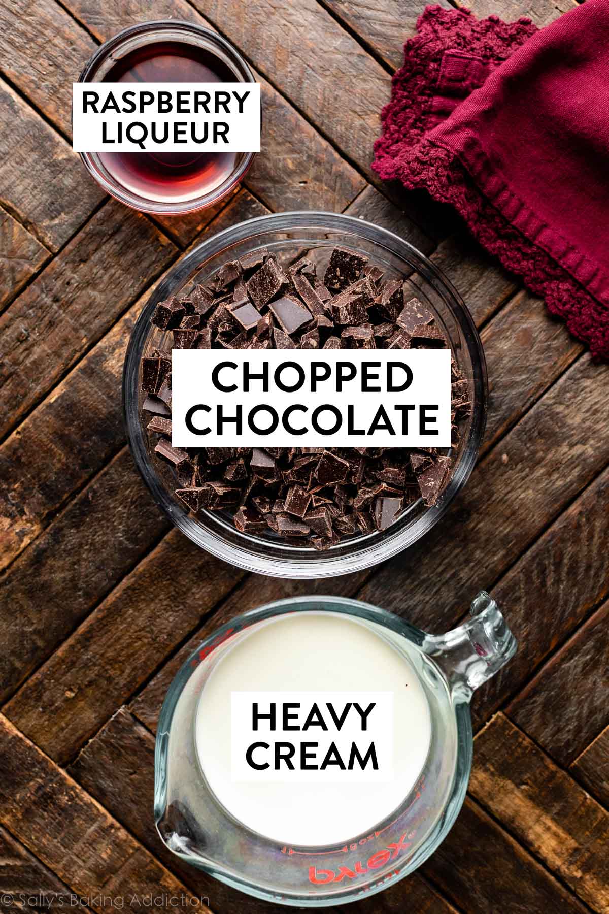 chopped chocolate, heavy cream, and raspberry liqueur in separate bowls on wooden surface.