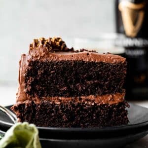 slice of Guinness chocolate cake with chocolate frosting on two stacked black plates.