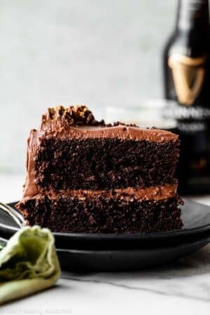 slice of Guinness chocolate cake with chocolate frosting on two stacked black plates.