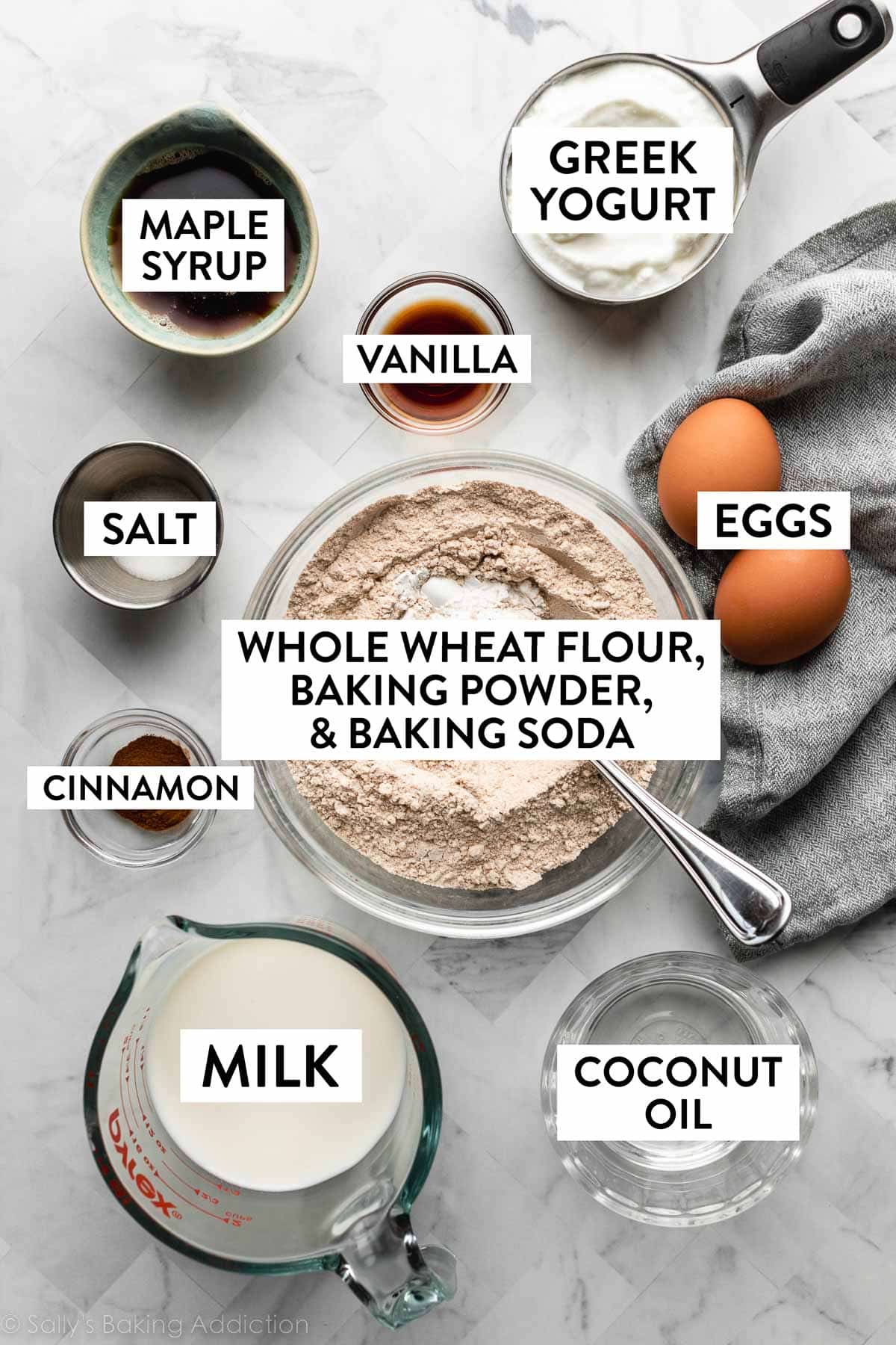 ingredients in bowls on counter including whole wheat flour, coconut oil, Greek yogurt, and maple syrup.