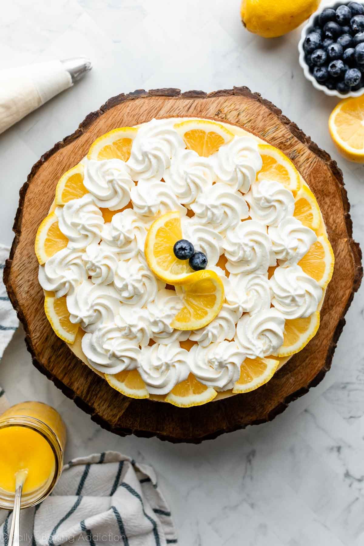 lemon cheesecake with piped whipped cream and lemon slices sitting on wooden cake stand.