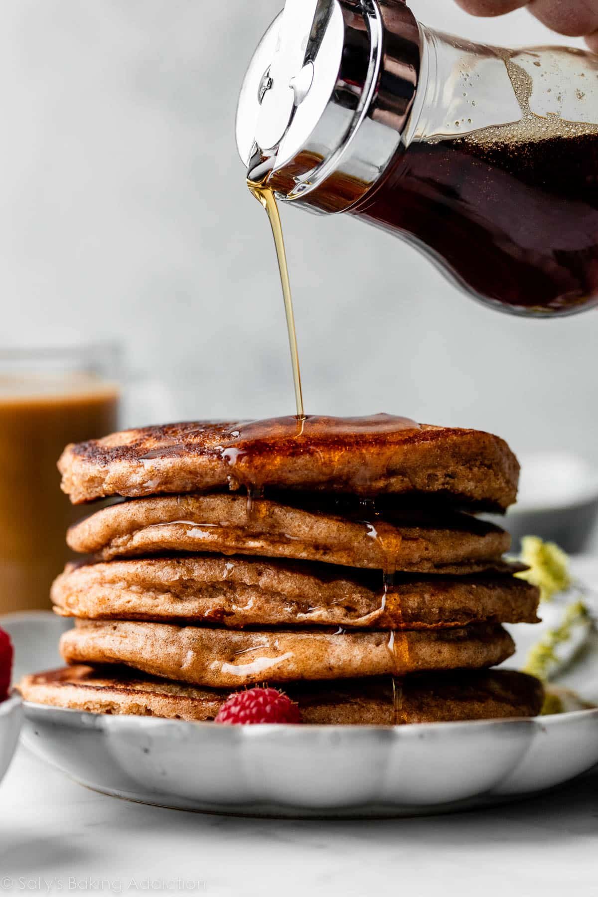 maple syrup being poured on a stack of pancakes on gray plate.