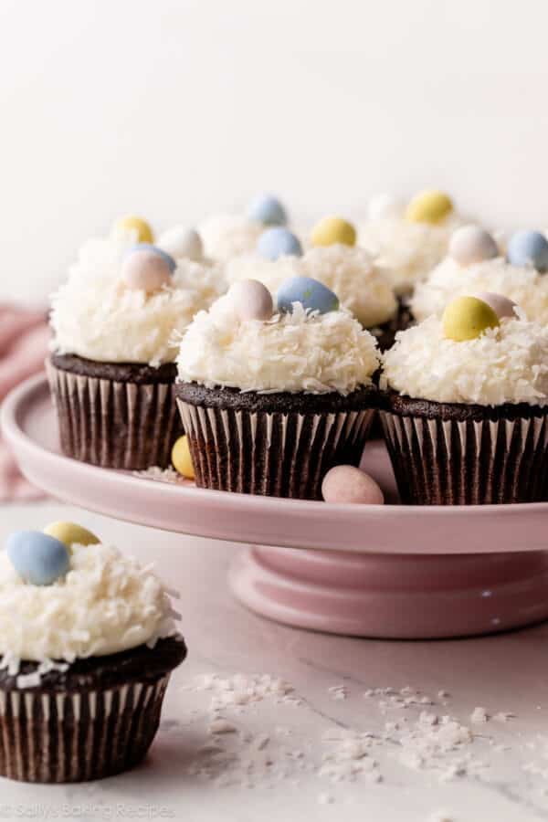 chocolate cupcakes with coconut frosting and egg candies arranged on pink cake stand.