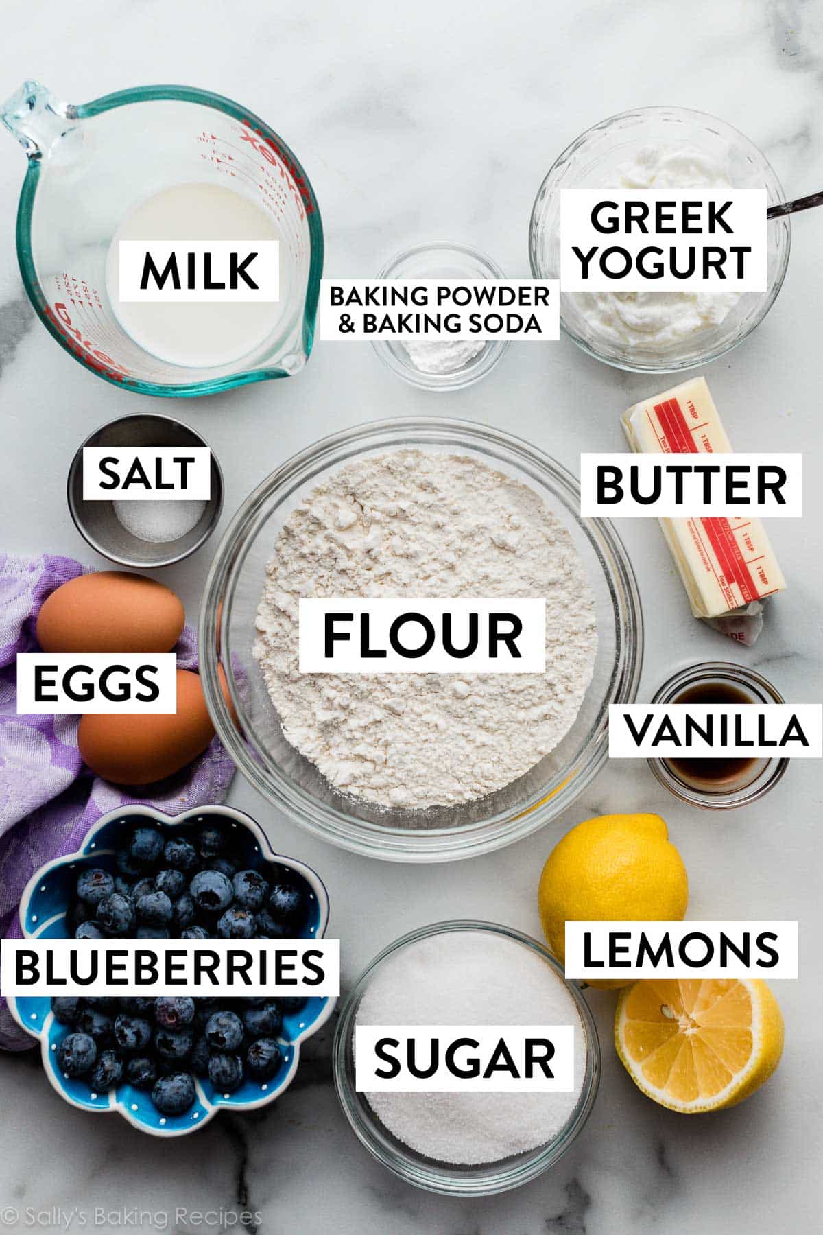 ingredients on marble counter including butter, yogurt, lemon, blueberries, and eggs.
