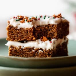 stack of 2 cream cheese frosted gingerbread cookie bars on green plates.