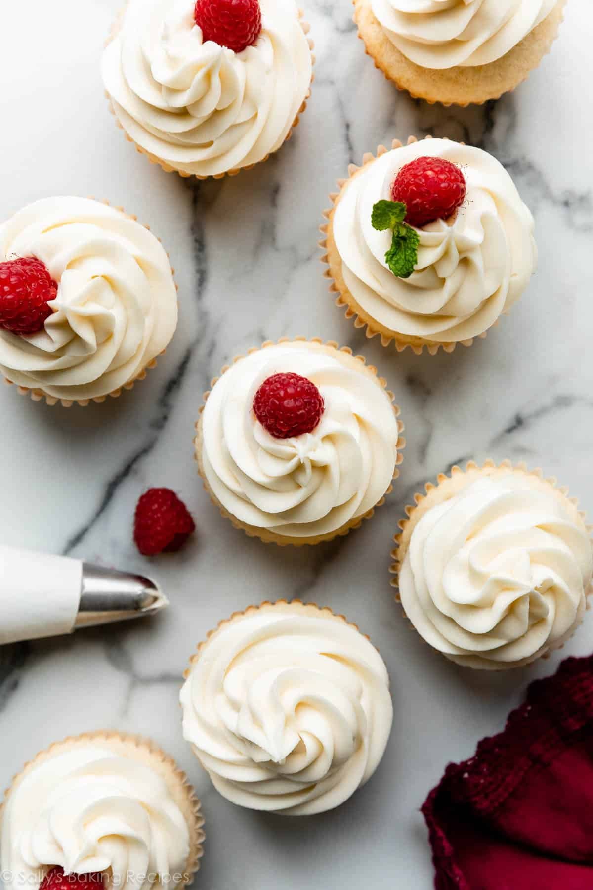 overhead image of cupcakes frosted with white chocolate buttercream and some garnished with a fresh raspberry.