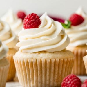 white chocolate buttercream frosting swirled on cupcake with raspberry and fresh mint garnish.