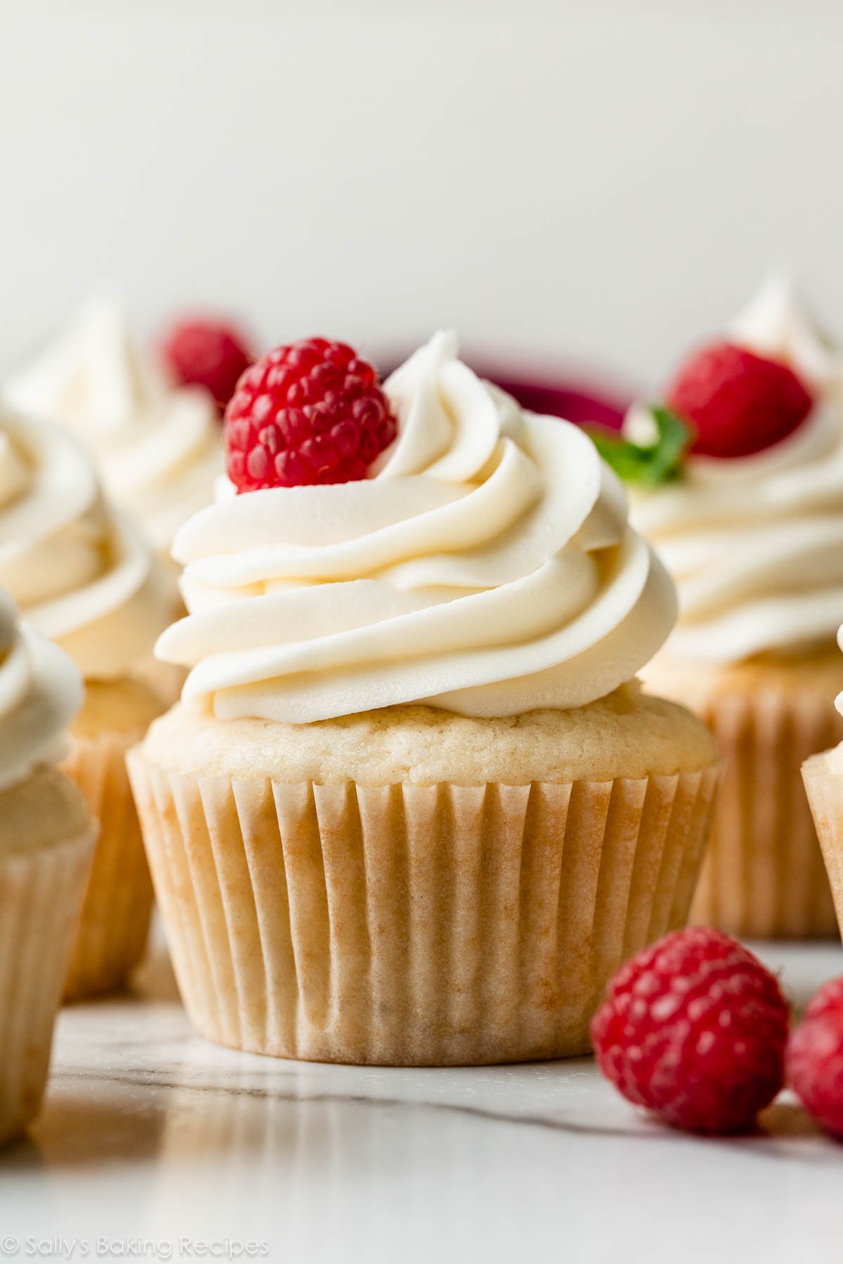 white chocolate buttercream frosting swirled on cupcake with raspberry and fresh mint garnish.