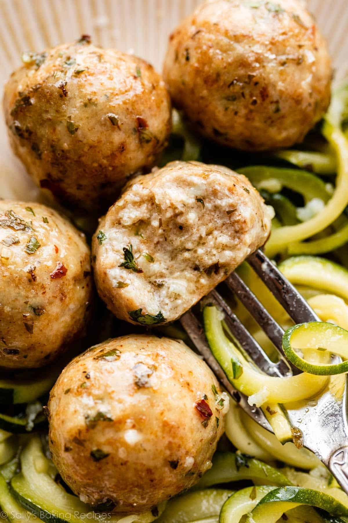 close-up of a chicken meatball with bite taken out of it sitting on a bed of zucchini noodles.