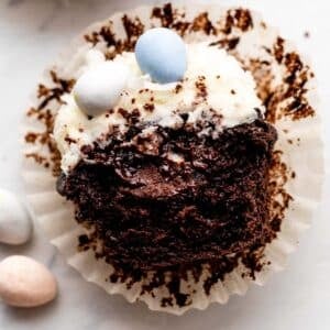 chocolate cupcake split in half to show ganache center and coconut cream cheese frosting on top.