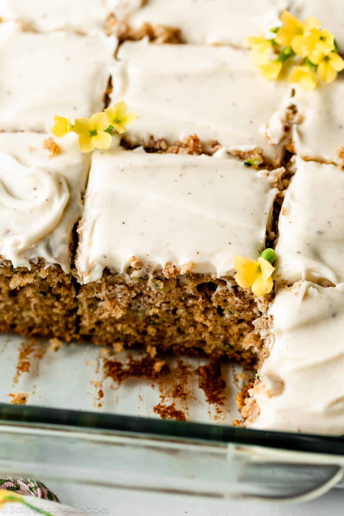 zucchini sheet cake in glass cake pan with yellow flowers as garnish on top.