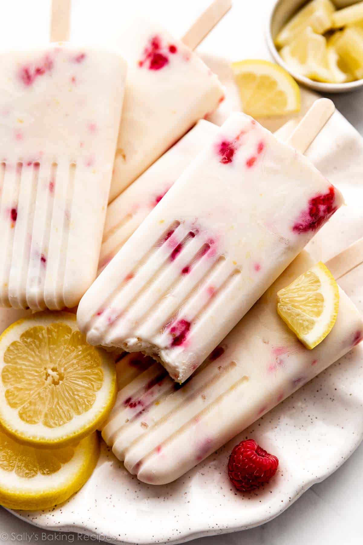 creamy lemon popsicles with raspberries inside on plate with fresh lemon slices.