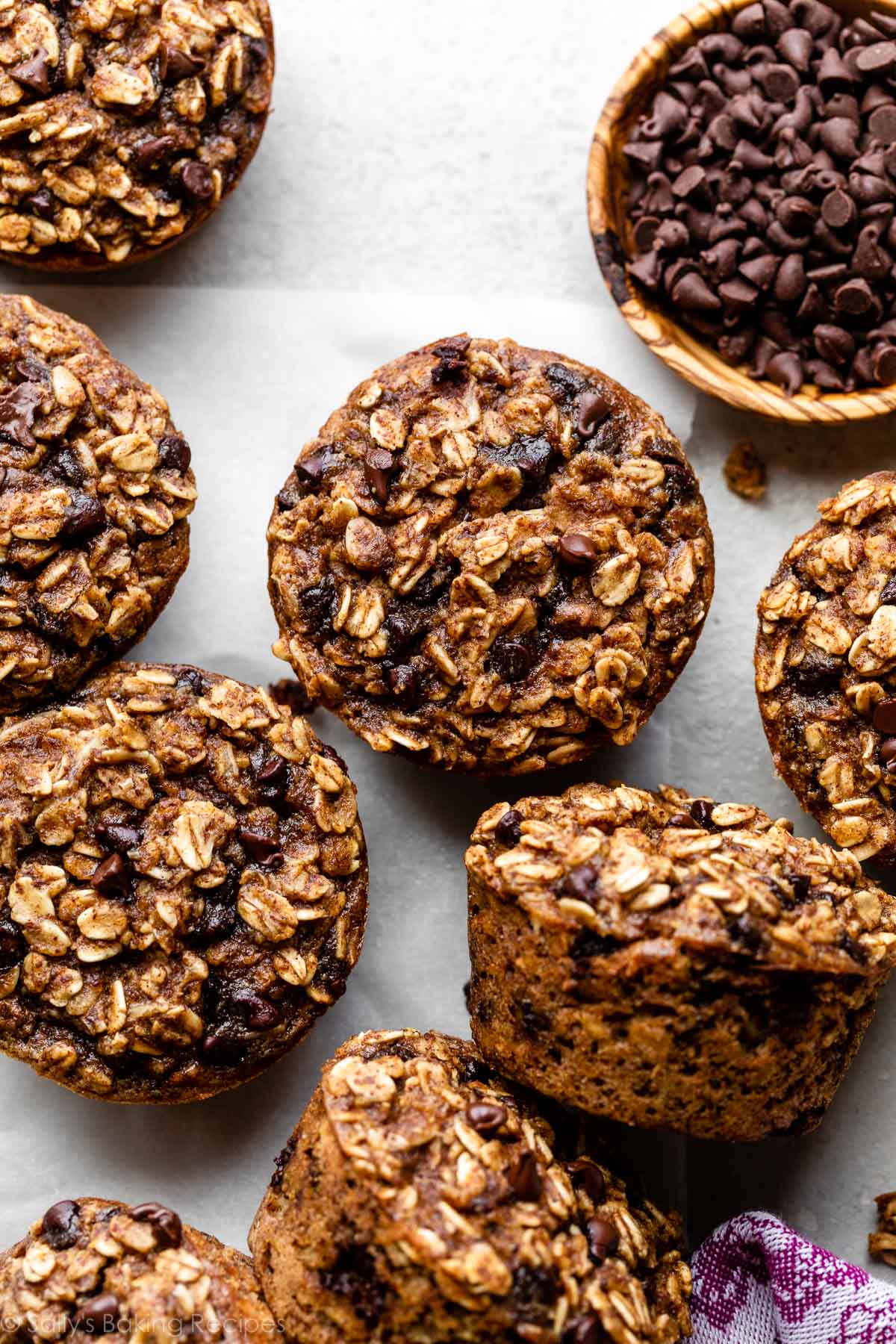 chocolate chip baked oatmeal cups on gray backdrop with wooden bowl of mini chocolate chips.