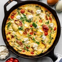 Mediterranean-inspired spinach and tomato frittata in cast iron skillet.
