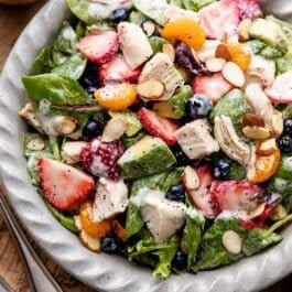 salad in gray dish including chicken, strawberries, mandarin oranges, blueberries, spinach, and avocado with poppy seed dressing on top.
