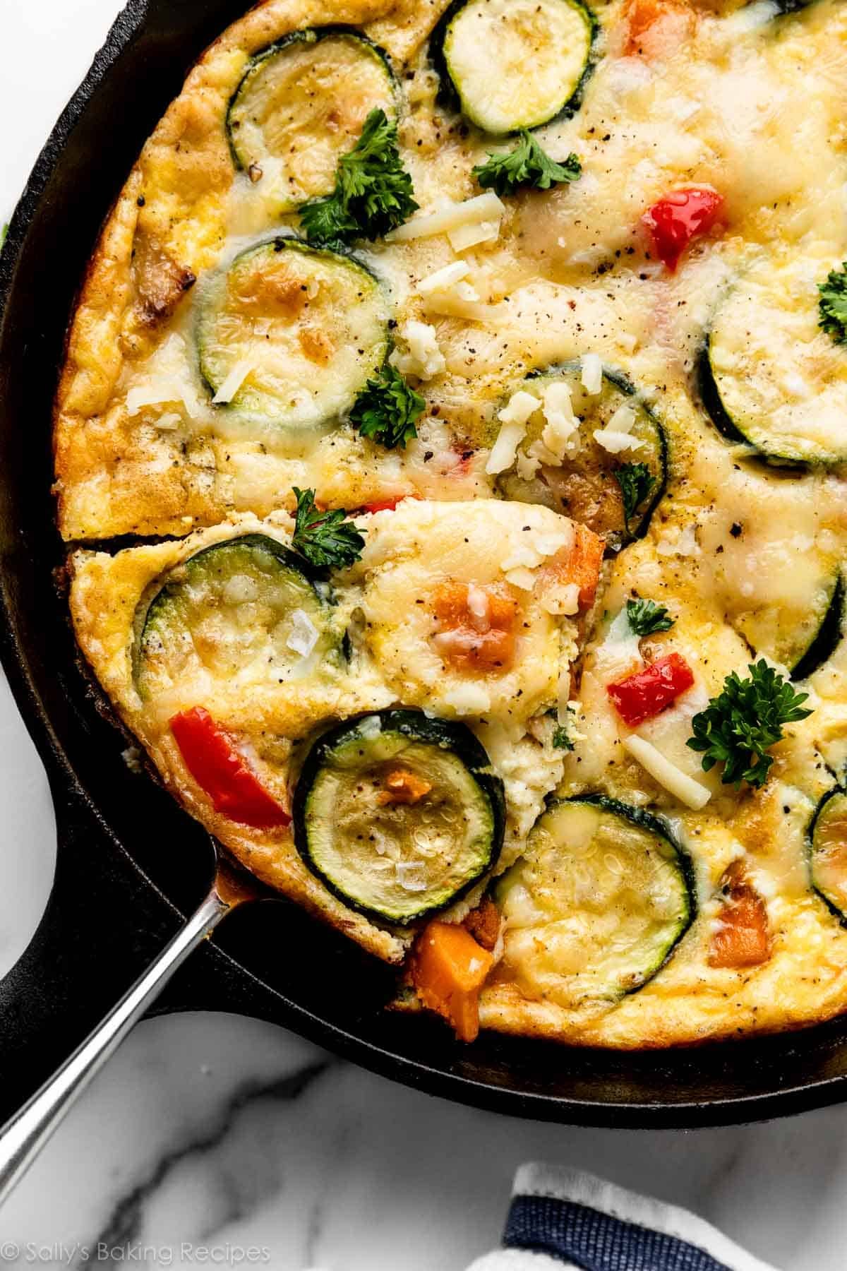 vegetable frittata in cast iron skillet with slice being removed.