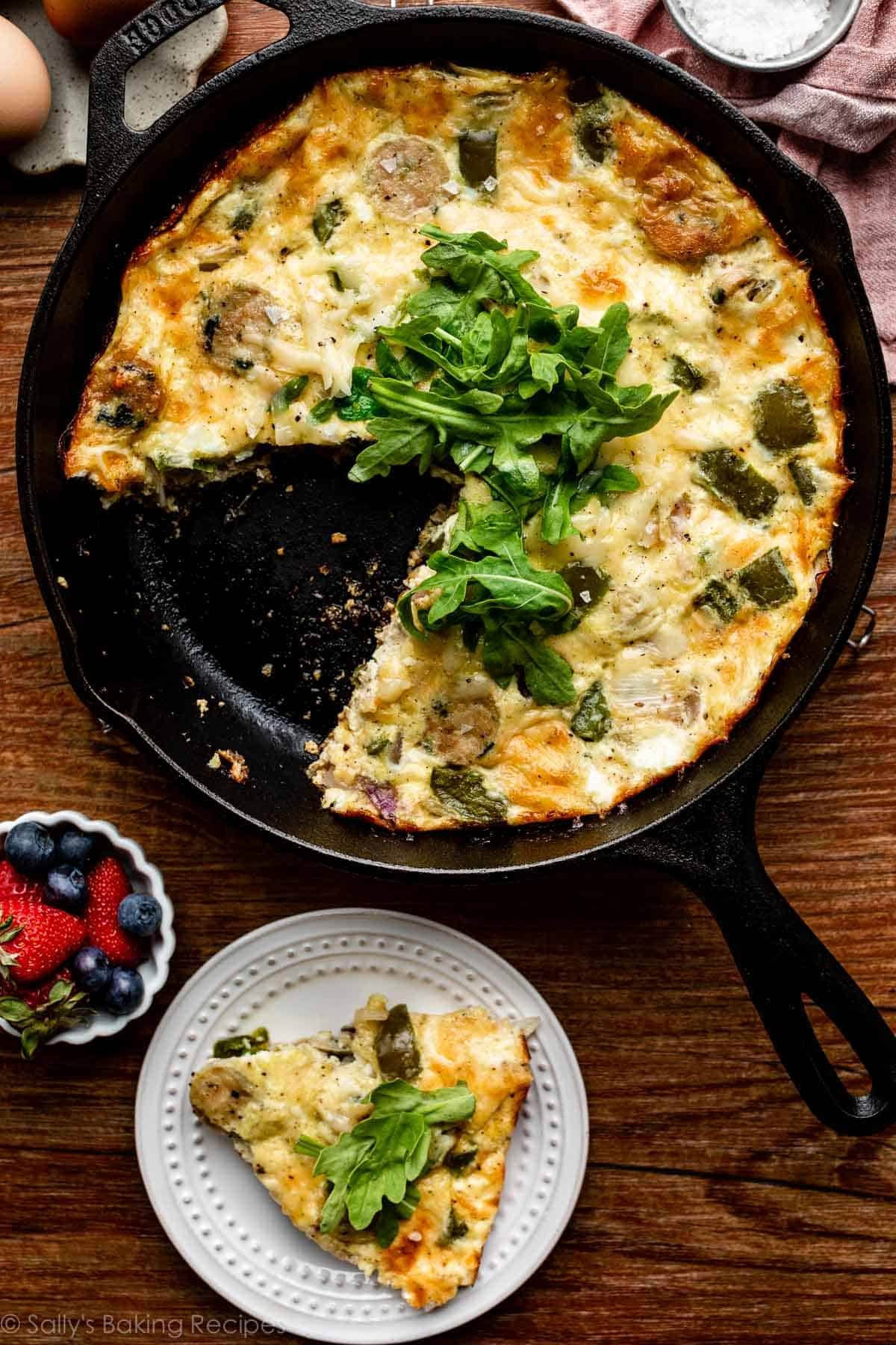 chicken sausage and green pepper frittata with fresh arugula on top in cast iron skillet.