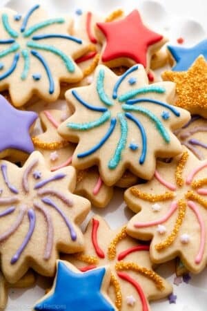 sugar cookies decorated like fireworks and stars with blue, red, pink, and purple icing with shimmery sprinkles on top.