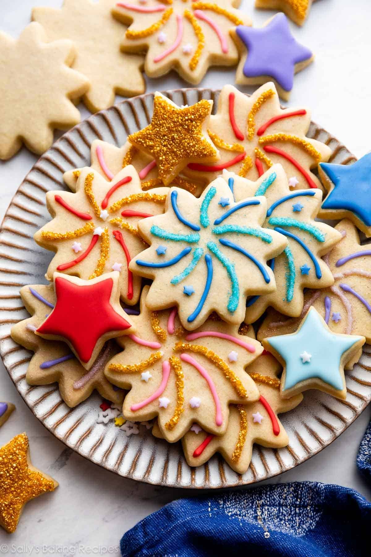 sugar cookies decorated like fireworks and stars with blue, red, pink, and purple icing on top arranged on gray plate.