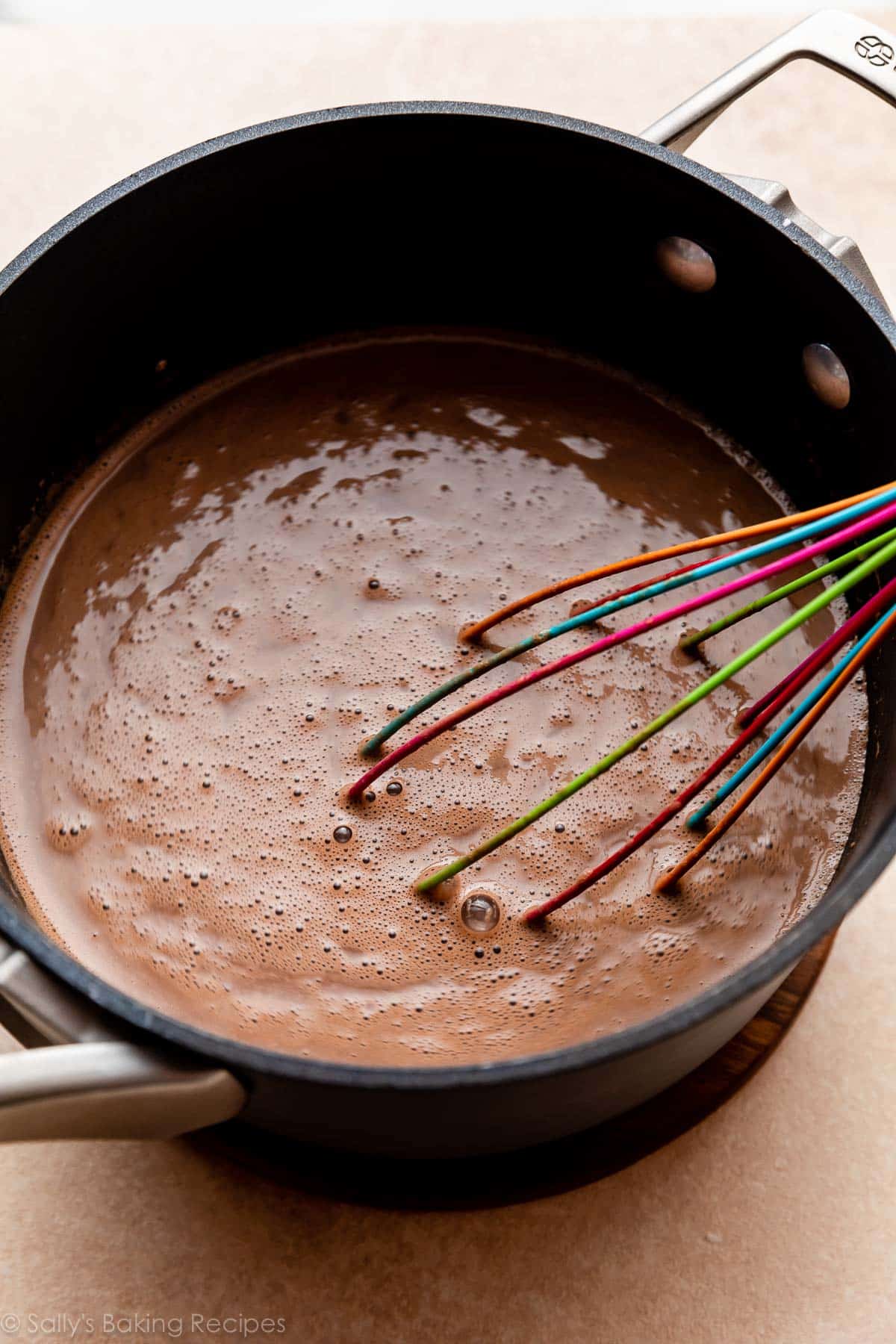 chocolate liquid mixture and rainbow whisk in saucepan.
