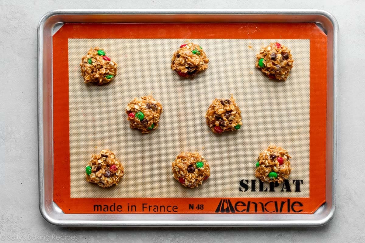 scoops of M&M oatmeal cookie dough on silicone baking mat-lined baking sheet.