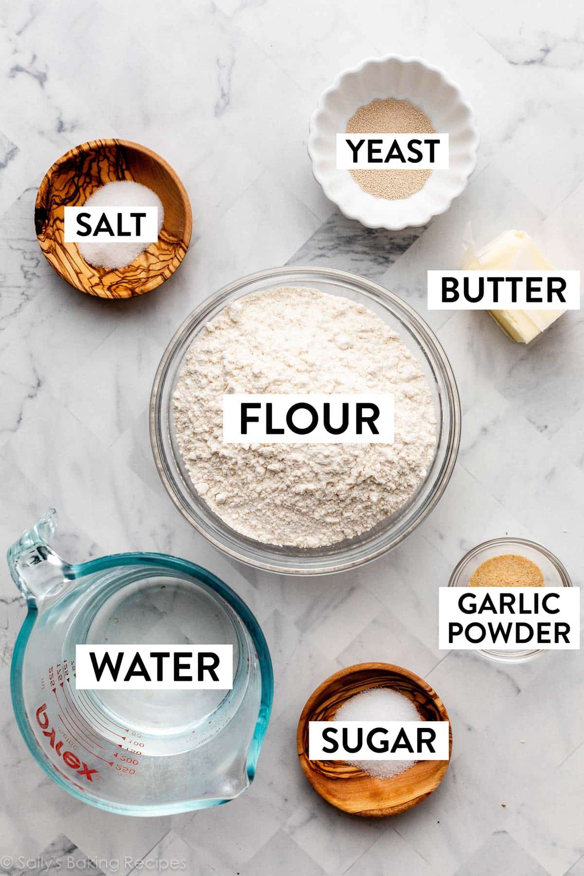 ingredients in bowls on counter including flour, butter, garlic powder, sugar, water, salt, and yeast.