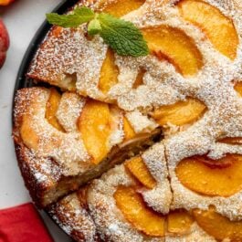 peach cake cut into slices sitting on bottom of springform pan.