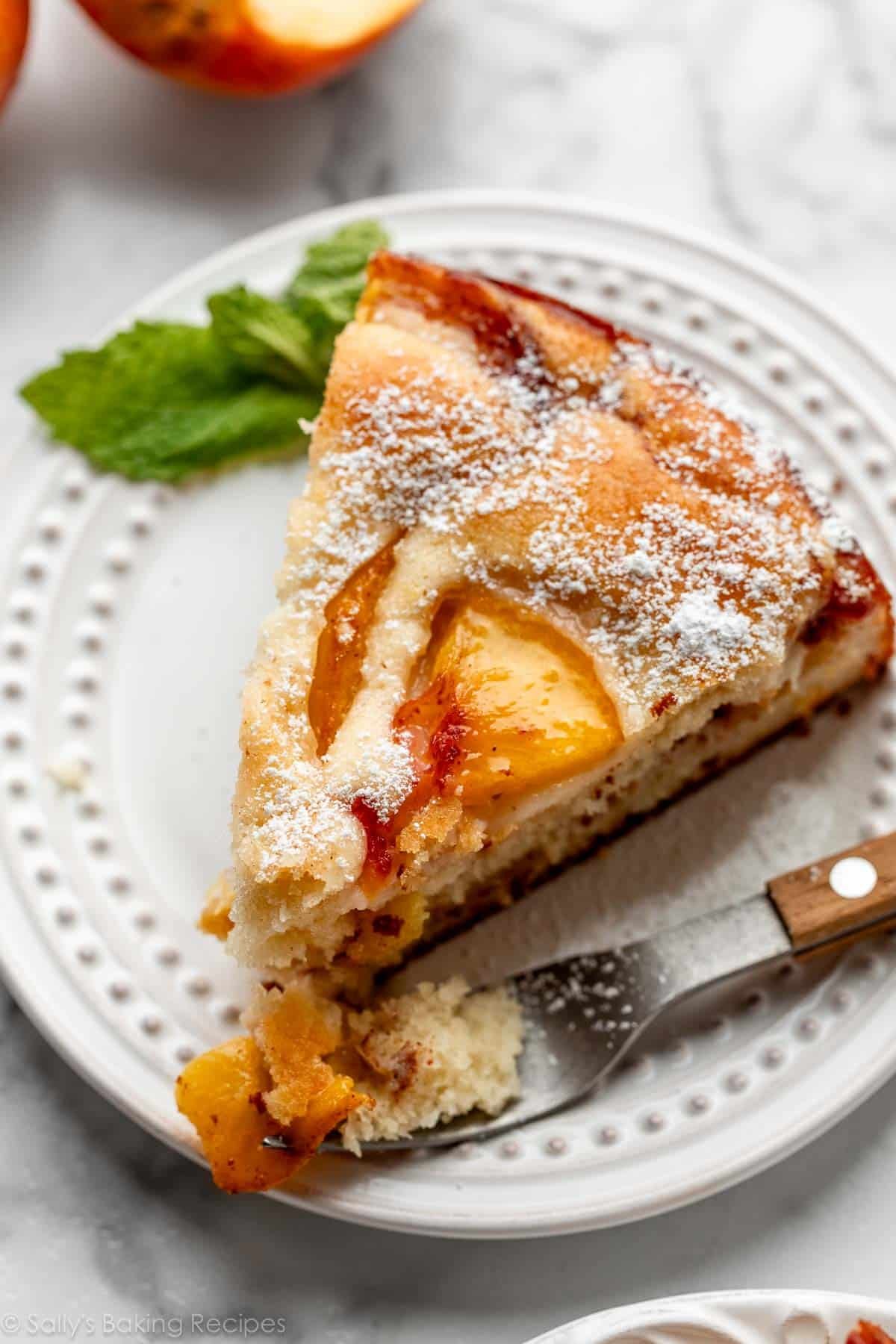 slice of fresh peach cake with confectioners' sugar on top on white plate.