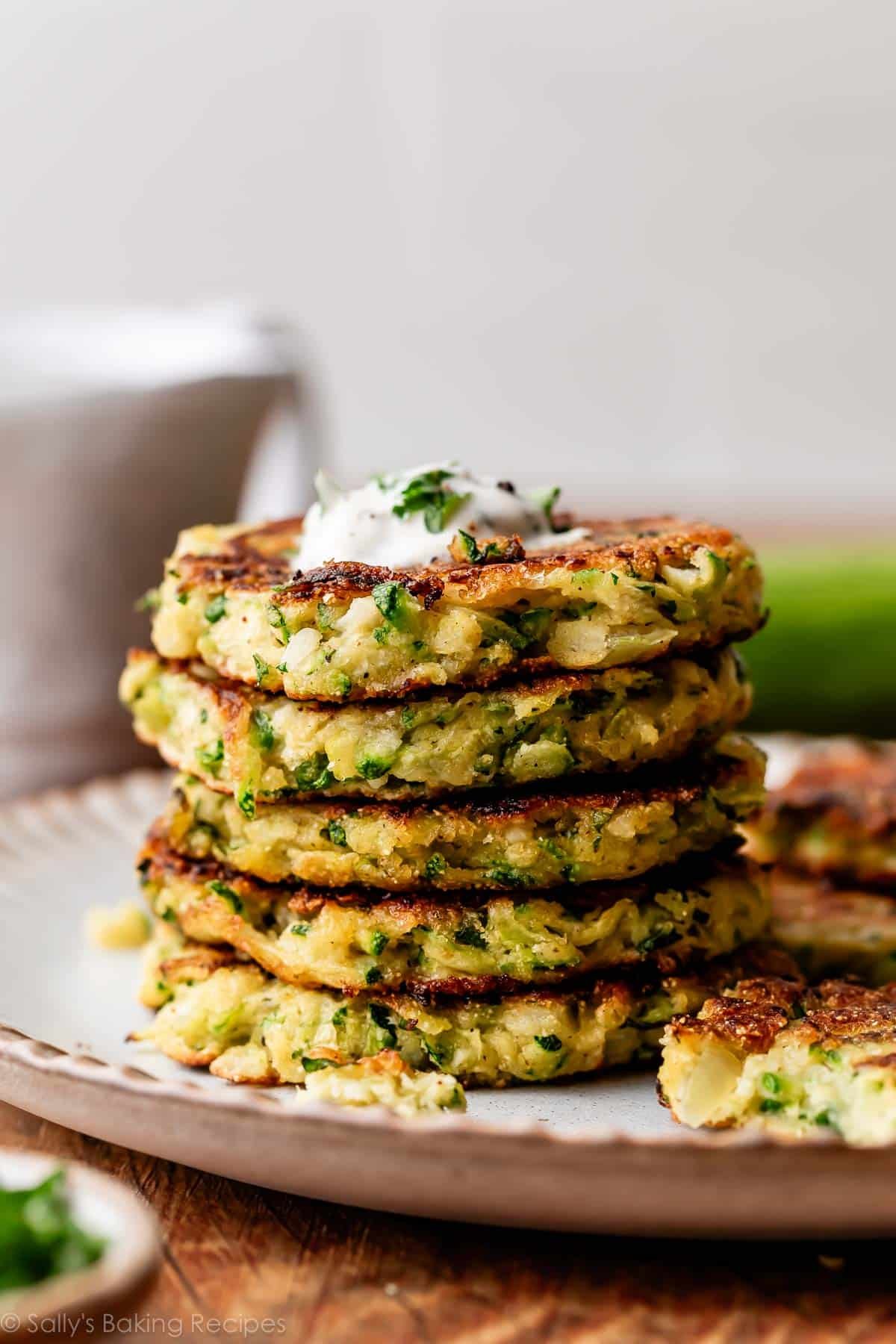 stack of zucchini fritters on gray plate with dollop of Greek yogurt sauce on top.