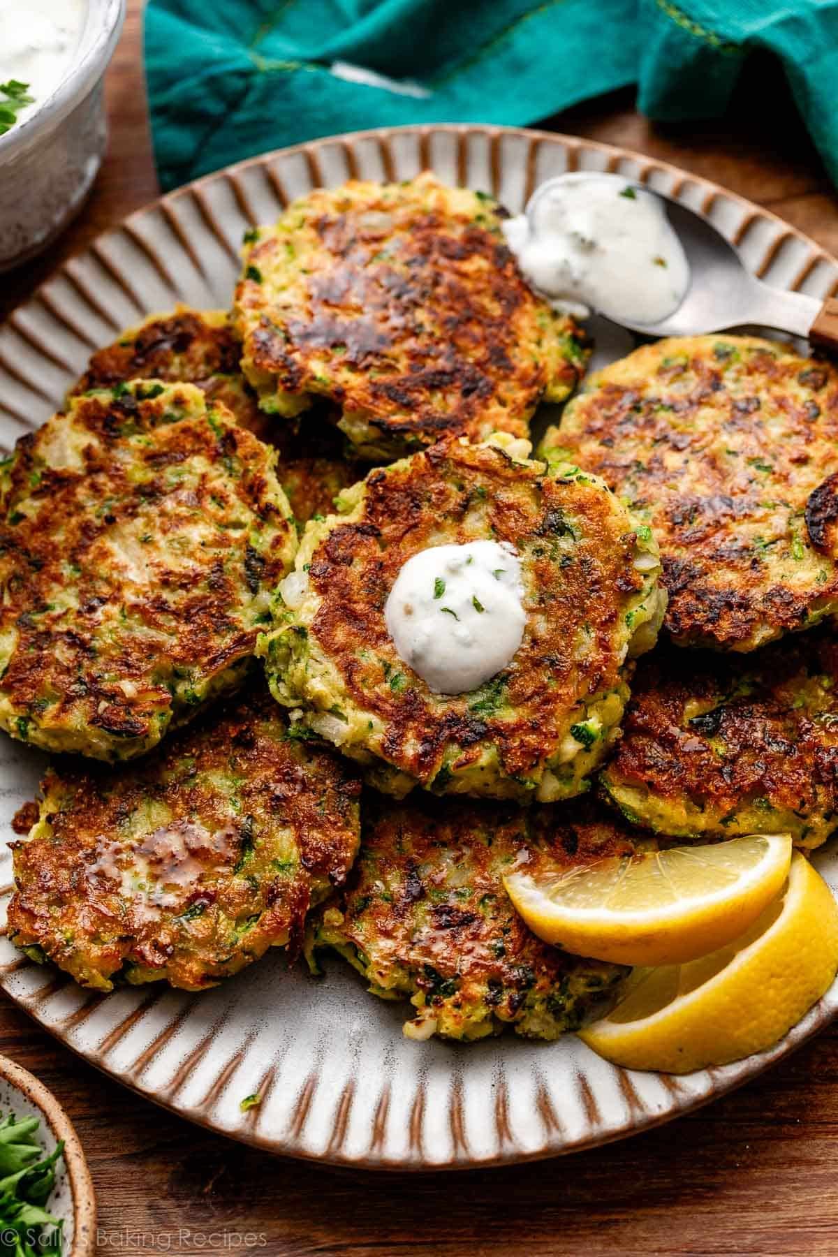 savory zucchini fritter cakes on gray plate with garlic herb Greek yogurt sauce on top of one.