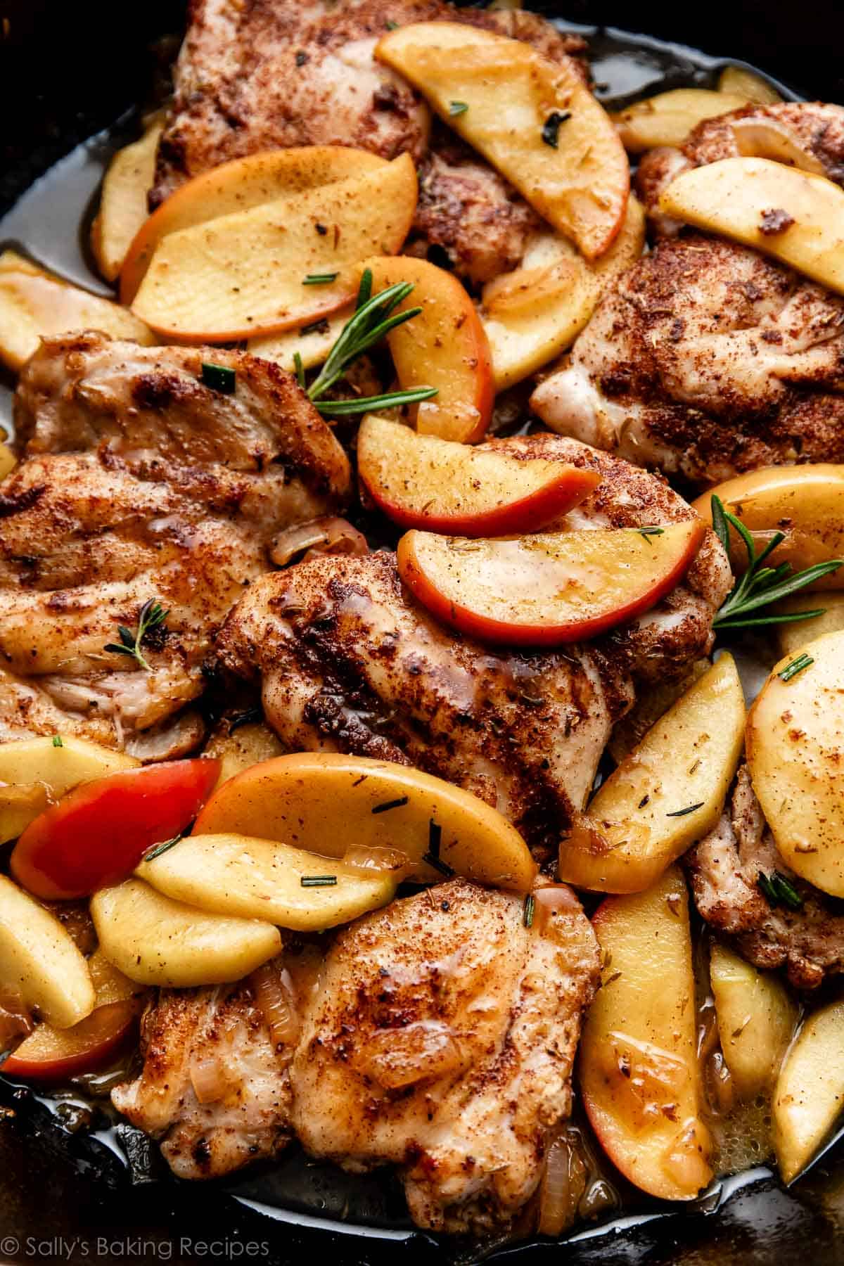 close up photo of apple cider chicken with apples and rosemary in skillet.