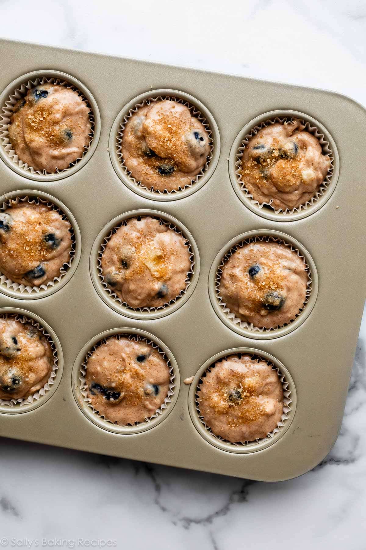 blueberry muffin batter in lined gold muffin pan.