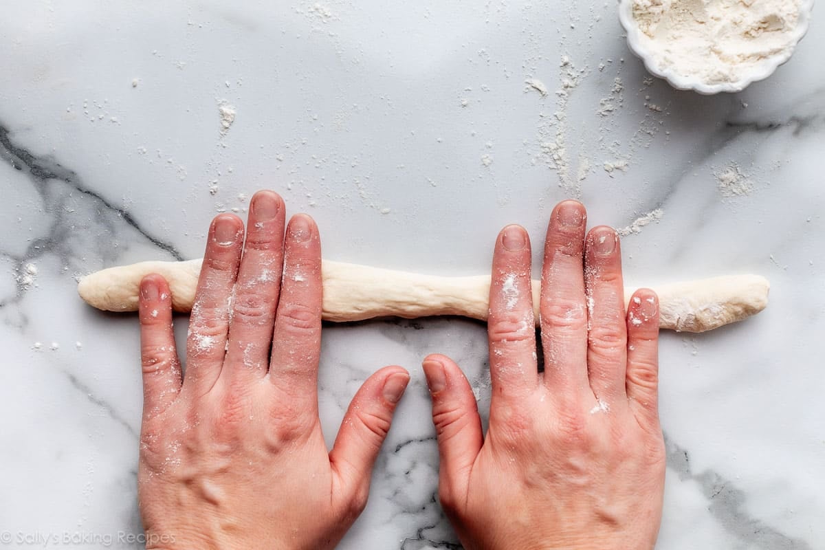 hands rolling rope of dough on marble counter.