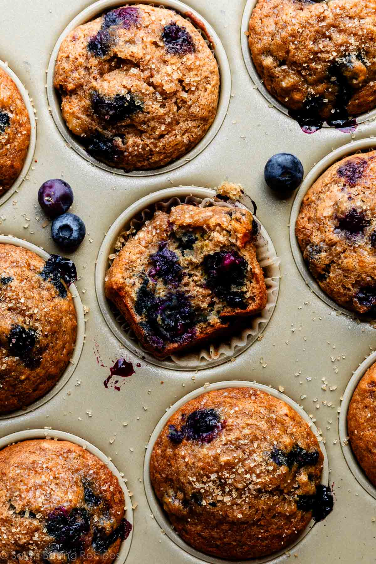 baked healthy blueberry banana muffins with one cut open in gold muffin pan.