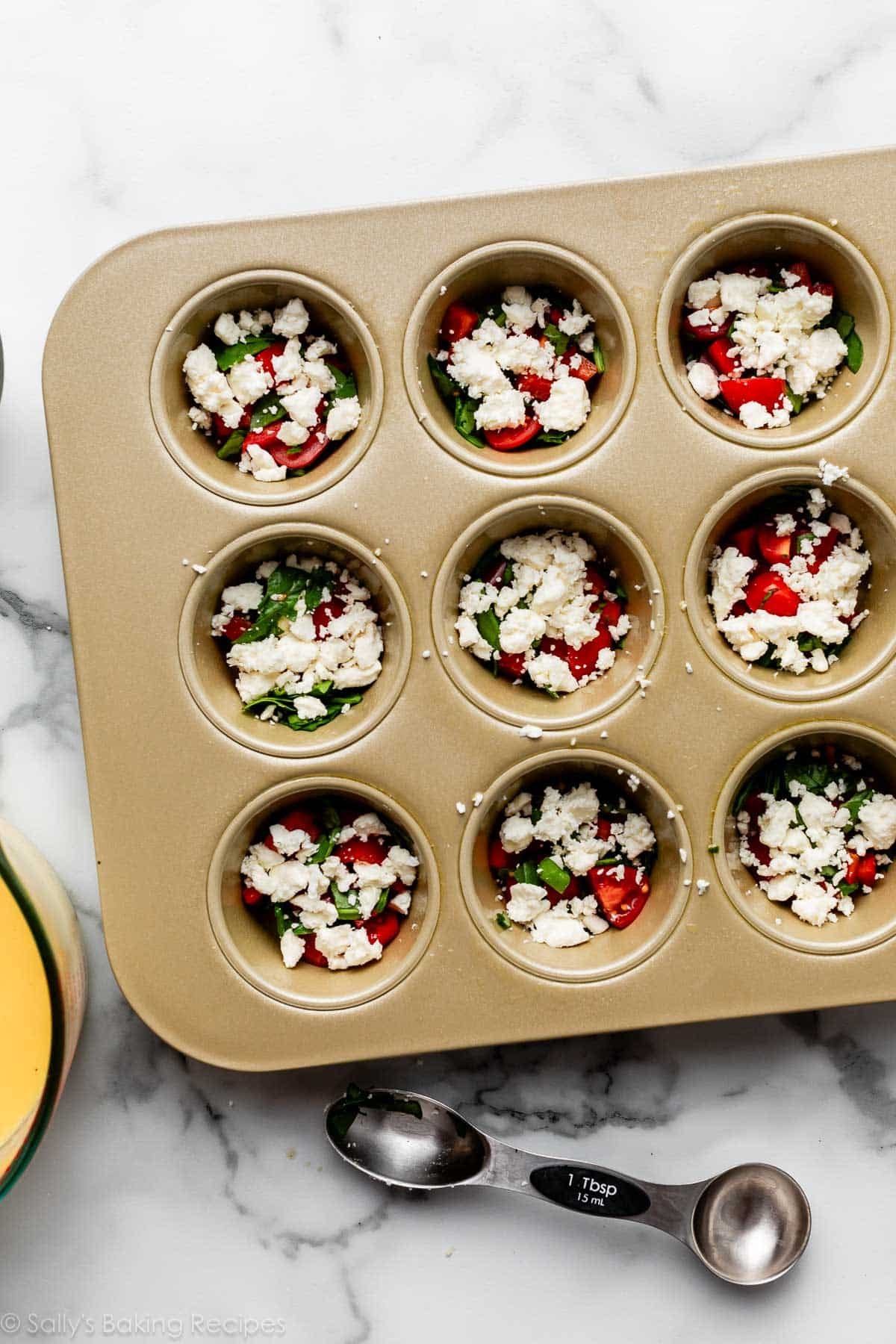 feta cheese, red pepper, and spinach piled in muffin pan.