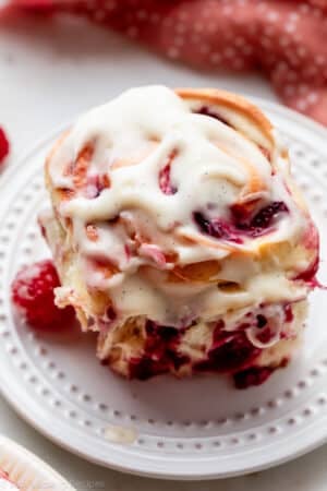 raspberry sweet roll with cream cheese icing on white plate.